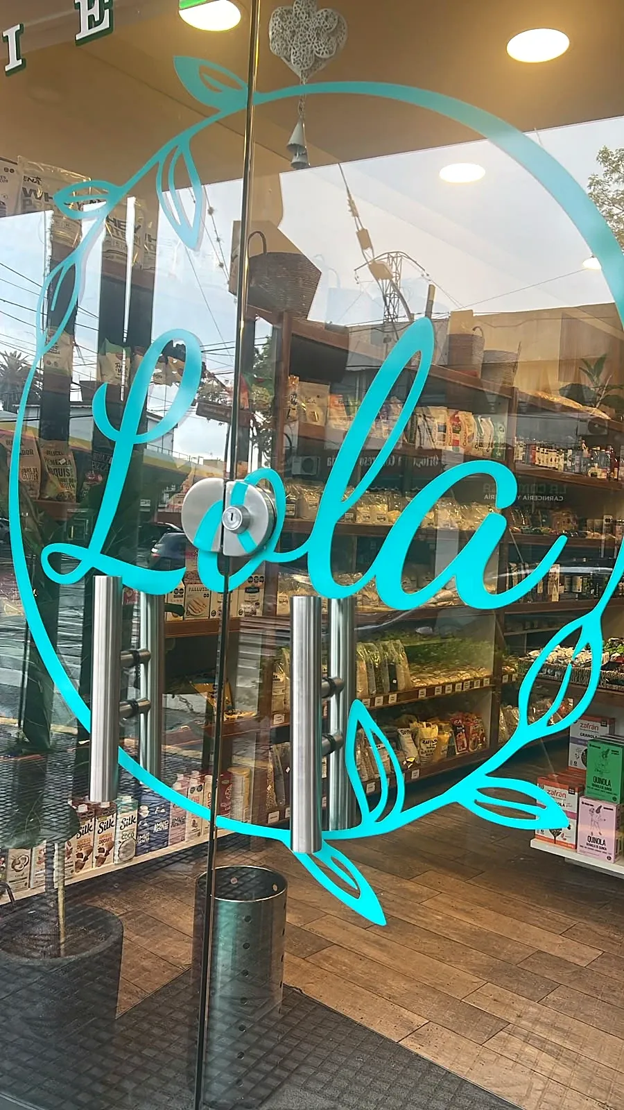Puerta de vidrio de La Almacén de Lola con el logo, y las góndolas de madera del otro lado