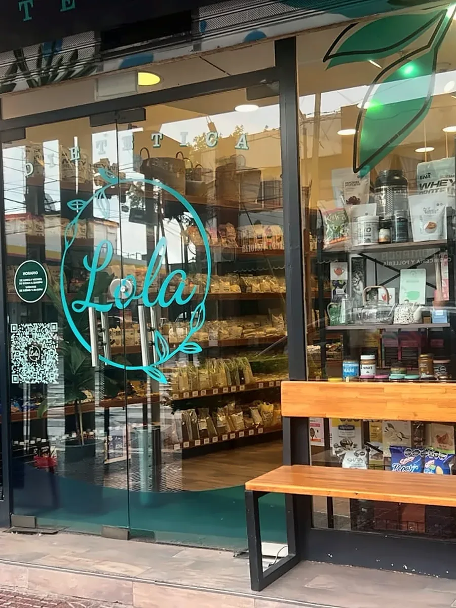 Vidriera con el logo de Lola, un banco de madera y plantas en la entrada